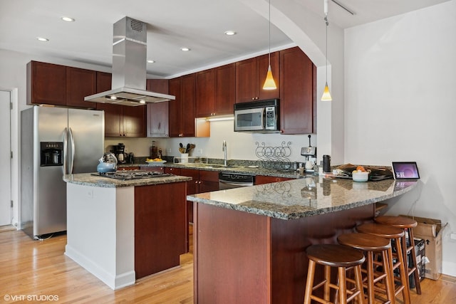 kitchen with dark stone counters, hanging light fixtures, appliances with stainless steel finishes, island range hood, and kitchen peninsula