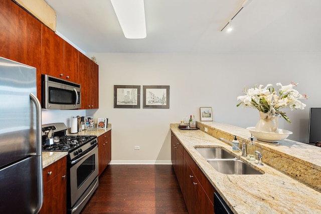 kitchen featuring dark wood-type flooring, track lighting, sink, appliances with stainless steel finishes, and light stone counters