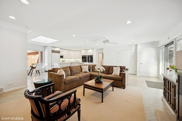 living room featuring ceiling fan, a skylight, and light wood-type flooring