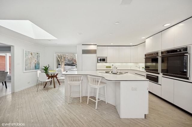 kitchen featuring a skylight, stainless steel microwave, white cabinetry, and black oven