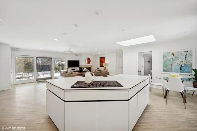 kitchen featuring light hardwood / wood-style floors, black electric stovetop, a skylight, white cabinetry, and ceiling fan