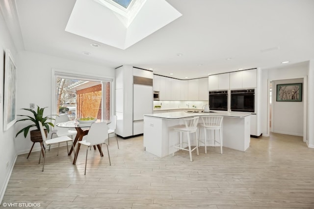 kitchen with white cabinets, a breakfast bar, a skylight, and a center island