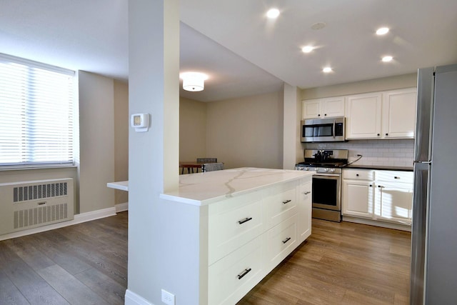 kitchen with white cabinets, stainless steel appliances, radiator heating unit, and tasteful backsplash