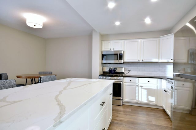 kitchen featuring white cabinets, appliances with stainless steel finishes, dark stone countertops, tasteful backsplash, and light wood-type flooring