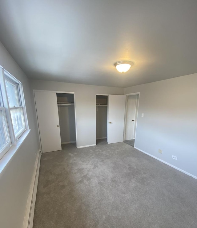 unfurnished bedroom featuring dark colored carpet, baseboard heating, and multiple closets