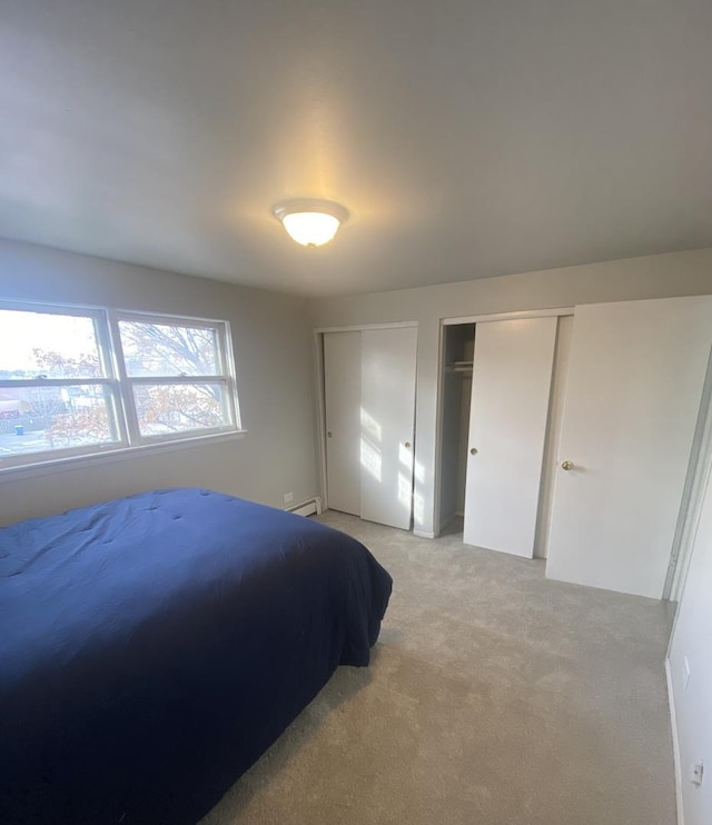 carpeted bedroom featuring a baseboard radiator and multiple closets