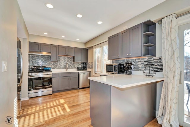 kitchen featuring light hardwood / wood-style floors, kitchen peninsula, appliances with stainless steel finishes, and decorative backsplash