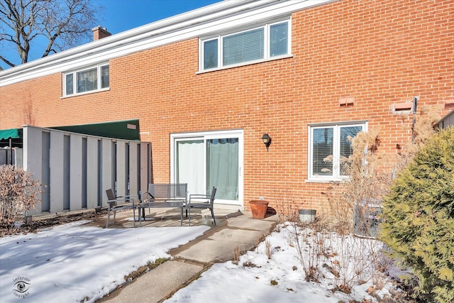 snow covered rear of property with a patio area