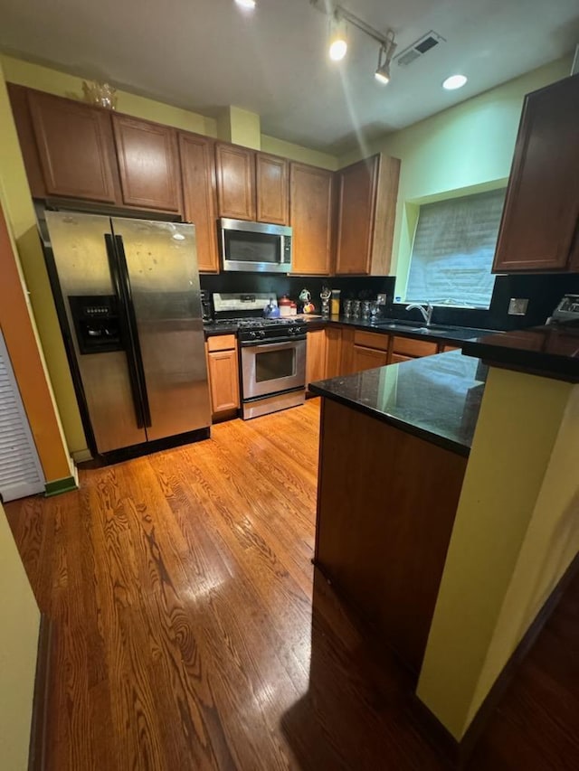 kitchen with appliances with stainless steel finishes, rail lighting, light hardwood / wood-style floors, and sink