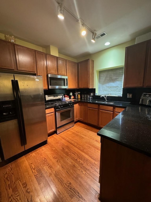 kitchen featuring sink, rail lighting, dark stone countertops, light hardwood / wood-style floors, and appliances with stainless steel finishes