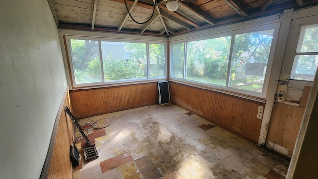 unfurnished sunroom with beamed ceiling, ceiling fan, wooden ceiling, and a wealth of natural light