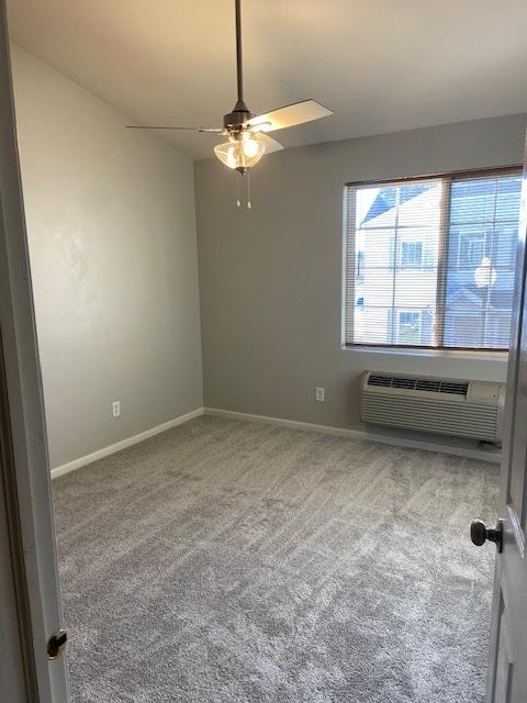 spare room featuring carpet flooring, a wall mounted AC, and ceiling fan