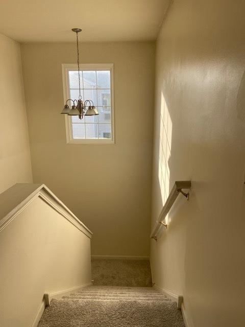 stairway with carpet floors and an inviting chandelier