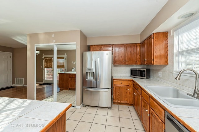 kitchen with backsplash, stainless steel appliances, sink, light tile patterned floors, and tile countertops