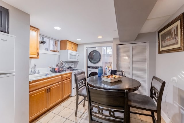 kitchen featuring stacked washer / drying machine, light tile patterned floors, white appliances, and sink