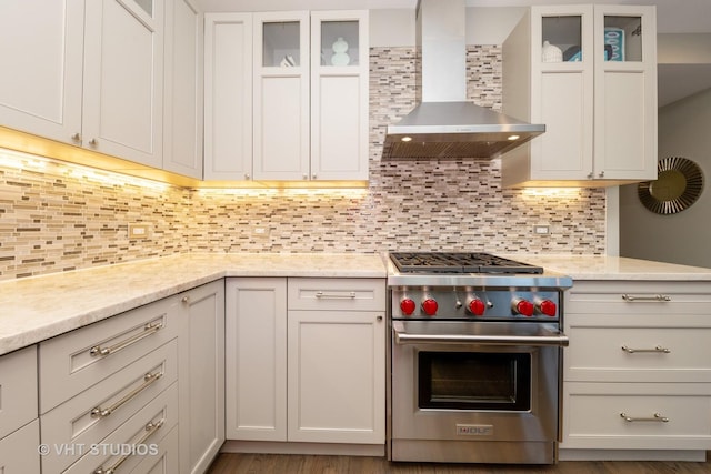 kitchen with light stone countertops, wall chimney range hood, white cabinetry, decorative backsplash, and luxury range