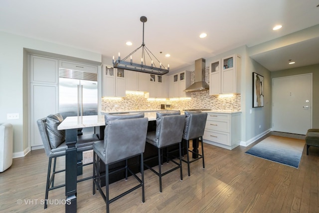 kitchen featuring decorative light fixtures, wall chimney range hood, a center island, white cabinetry, and light hardwood / wood-style flooring