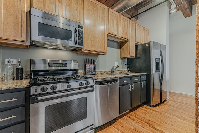 kitchen featuring light stone countertops, stainless steel appliances, sink, light brown cabinets, and light hardwood / wood-style flooring