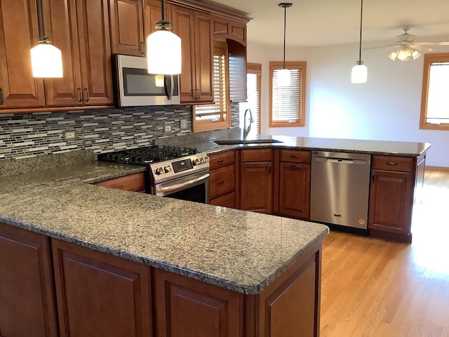 kitchen with kitchen peninsula, appliances with stainless steel finishes, ceiling fan, sink, and pendant lighting