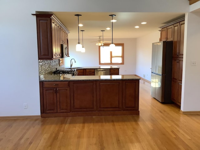 kitchen with stainless steel appliances, kitchen peninsula, dark stone counters, pendant lighting, and light wood-type flooring