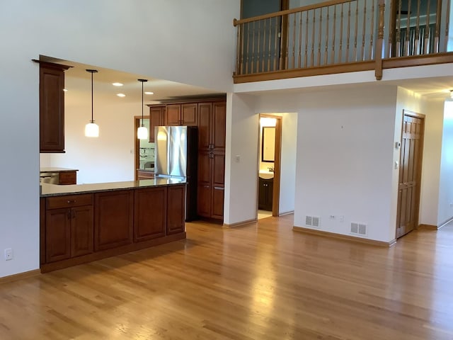 kitchen with stainless steel fridge, a towering ceiling, light hardwood / wood-style flooring, and hanging light fixtures