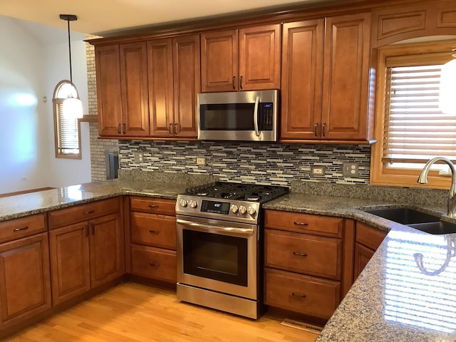 kitchen featuring sink, stainless steel appliances, dark stone countertops, light hardwood / wood-style floors, and decorative light fixtures