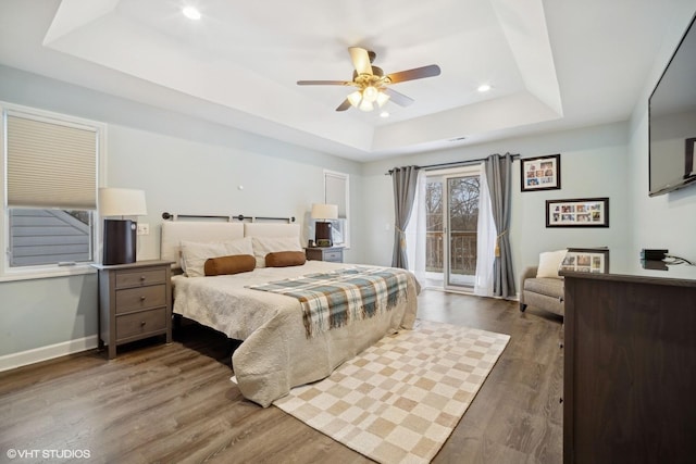 bedroom with ceiling fan, access to exterior, dark hardwood / wood-style flooring, and a raised ceiling