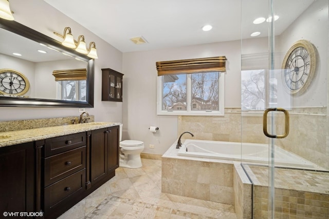 bathroom with tiled bath, a healthy amount of sunlight, vanity, and toilet