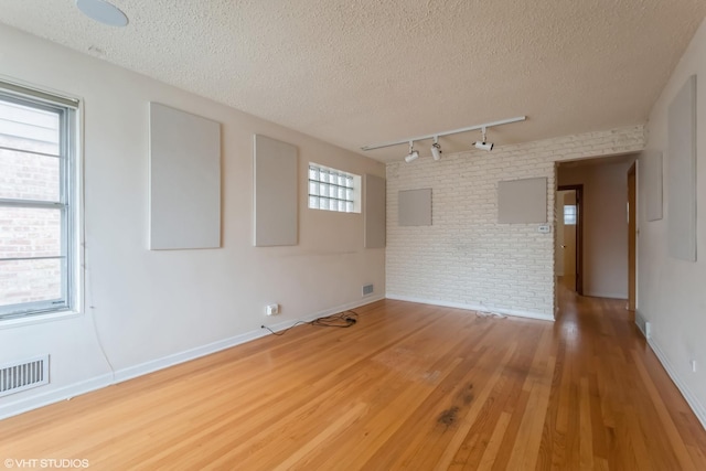 unfurnished room with wood-type flooring, rail lighting, a textured ceiling, and brick wall