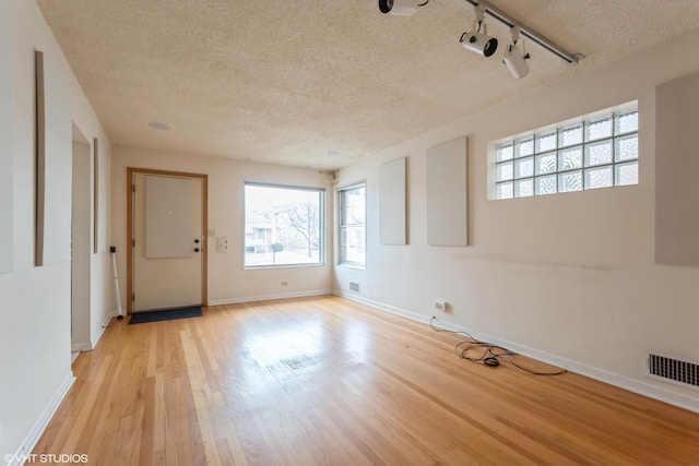 empty room featuring a textured ceiling, light hardwood / wood-style floors, and track lighting