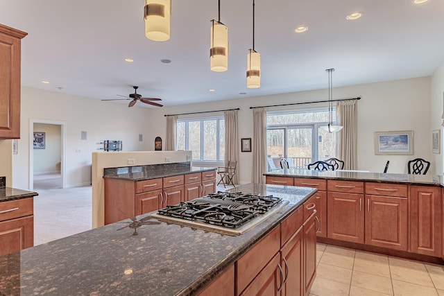 kitchen featuring ceiling fan, stainless steel gas cooktop, dark stone countertops, decorative light fixtures, and light tile patterned flooring