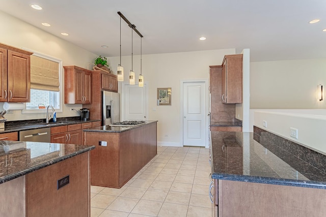 kitchen featuring appliances with stainless steel finishes, dark stone counters, sink, decorative light fixtures, and a center island