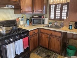 kitchen featuring backsplash, black gas stove, range hood, and sink