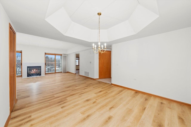 unfurnished living room with light wood-type flooring, a tray ceiling, and a chandelier