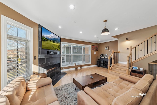 living room featuring a tiled fireplace, crown molding, and light hardwood / wood-style floors