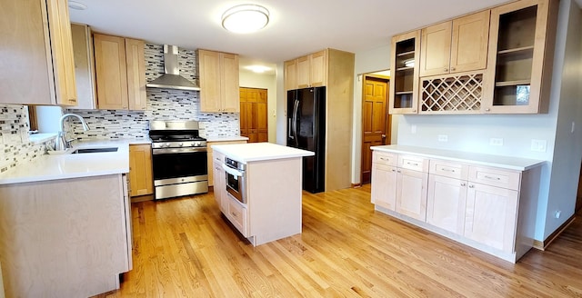 kitchen with stove, black fridge, wall chimney exhaust hood, sink, and a center island