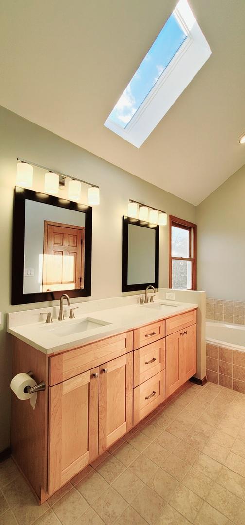 bathroom with vanity, a relaxing tiled tub, tile patterned floors, and vaulted ceiling