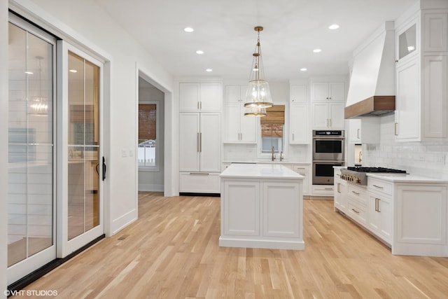 kitchen with custom exhaust hood, stainless steel appliances, decorative light fixtures, white cabinets, and a center island