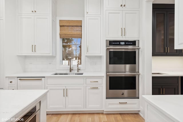 kitchen with decorative backsplash, stainless steel double oven, sink, dishwasher, and white cabinetry