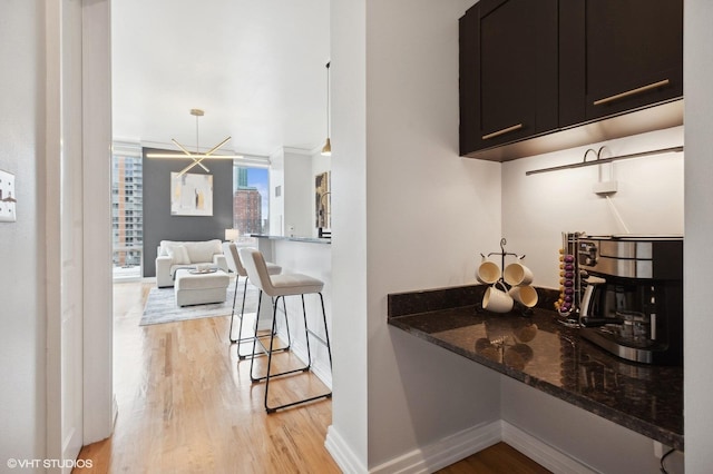 kitchen featuring a kitchen bar, crown molding, dark stone counters, and light hardwood / wood-style floors