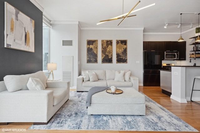 living room with crown molding, light hardwood / wood-style flooring, rail lighting, and an inviting chandelier