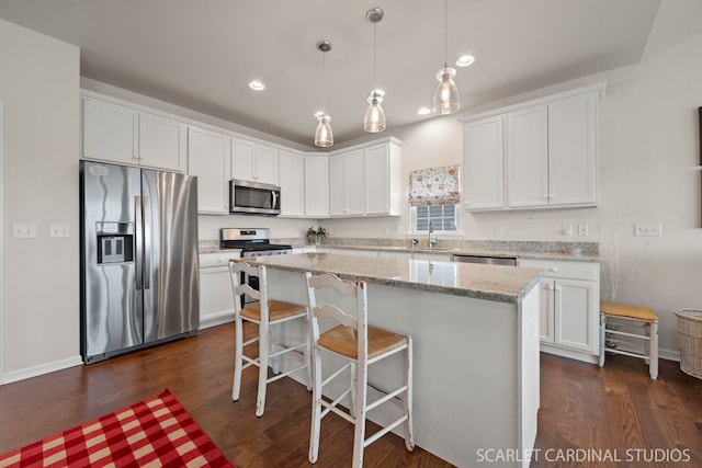 kitchen with decorative light fixtures, stainless steel appliances, white cabinetry, and a kitchen island