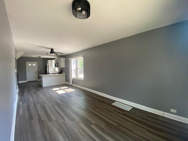 unfurnished living room featuring ceiling fan and dark wood-type flooring