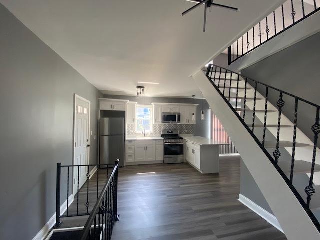 interior space featuring ceiling fan, dark wood-type flooring, backsplash, white cabinets, and appliances with stainless steel finishes