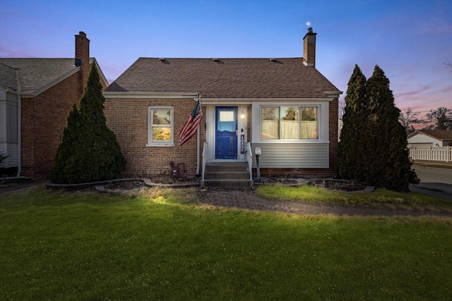 bungalow featuring roof with shingles, a chimney, entry steps, a front lawn, and brick siding