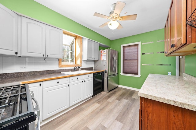 kitchen featuring light wood finished floors, a sink, decorative backsplash, appliances with stainless steel finishes, and white cabinetry