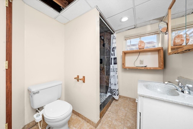 bathroom with toilet, baseboards, a shower stall, a paneled ceiling, and vanity