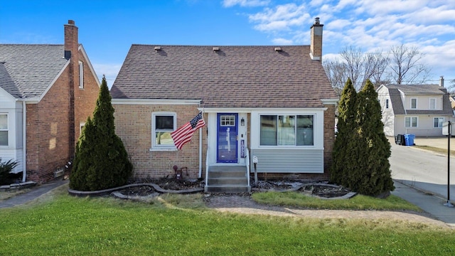 view of front of property featuring a front yard, brick siding, roof with shingles, and a chimney