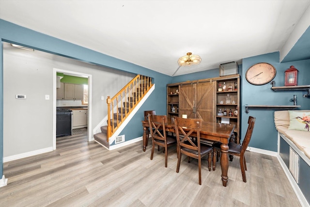 dining area featuring wood finished floors, visible vents, baseboards, stairs, and a barn door