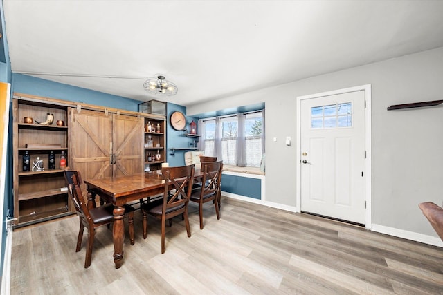 dining area featuring a barn door, baseboards, and light wood-style floors